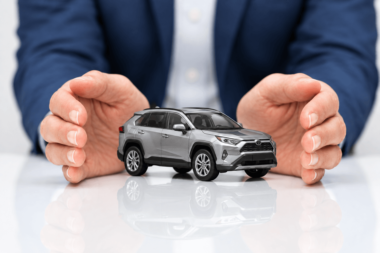 Hands cupped around a silver SUV model, illustrating auto insurance protection